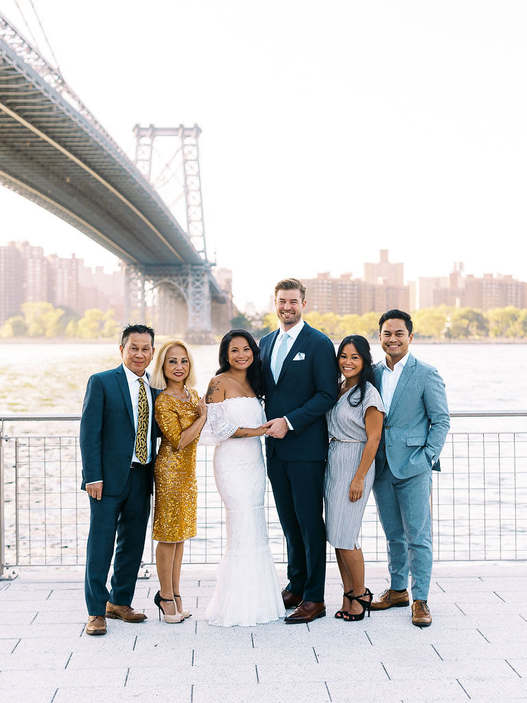 A newlywed couple and their families stand in front of the Williamsburg bridge on their wedding day.