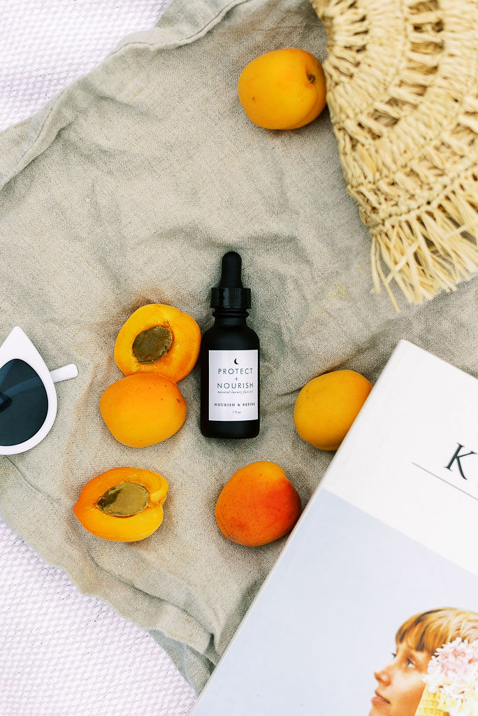 Peaches, a small bottle of face serum, Kinfolk magazine. and pair of white sunglasses lay on a gray blanket.