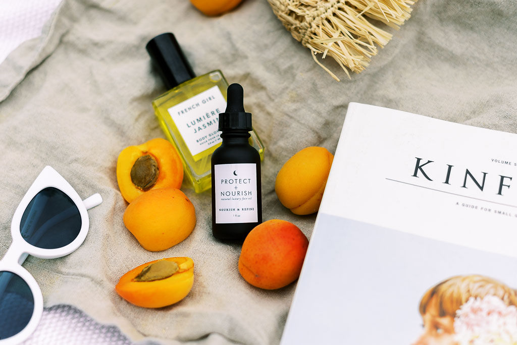 Peaches, two small bottles of face serum and body oil, Kinfolk magazine. and pair of white sunglasses lay on a gray blanket. Photographed by Washington DC and Virginia commercial photographer Kim Branagan.