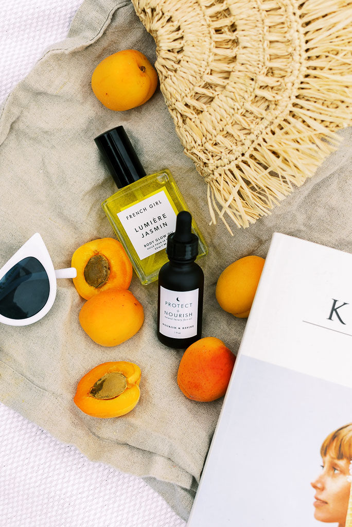 Peaches, two small bottles of face serum and body oil, Kinfolk magazine. a woven clutch bag, and pair of white sunglasses lay on a gray blanket. Photographed by Washington DC and Virginia commercial photographer Kim Branagan.