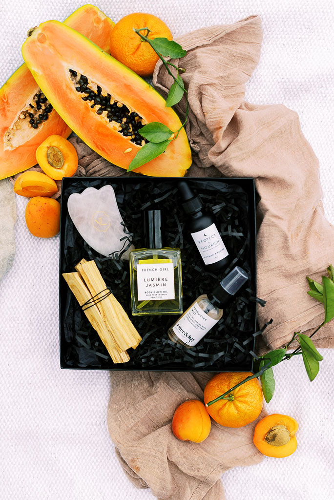 Verde Lusso's summer luxury clean beauty box lays open on a mauve picnic blanket, surrounded by summer citrus fruits. Photographed by east coast branding photographer Kim Branagan.