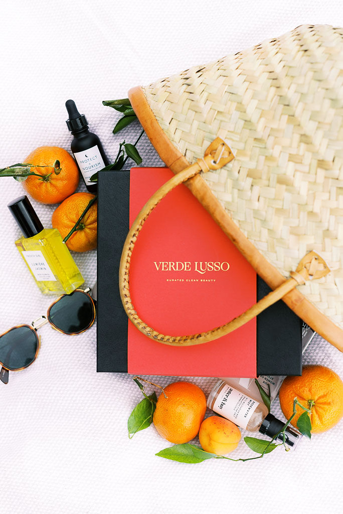 Verde Lusso beauty box with the company logo on the front of the box, laying next to a wicker tote bag, with oranges and the beauty products surrounding the bag. Photographed by Washington DC product photographer Kim Branagan.