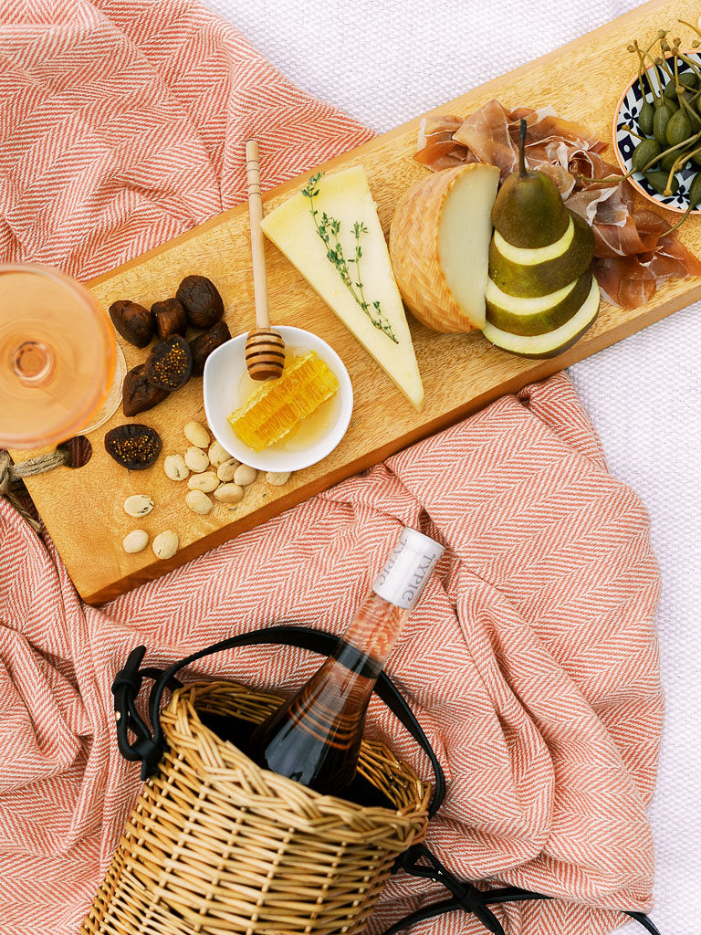 A charcuterie board with fruit, olives, cheese, meat, and nuts and a bottle of rose on a pink picnic blanket. Photographed by Washington DC brand photographer Kim Branagan.
