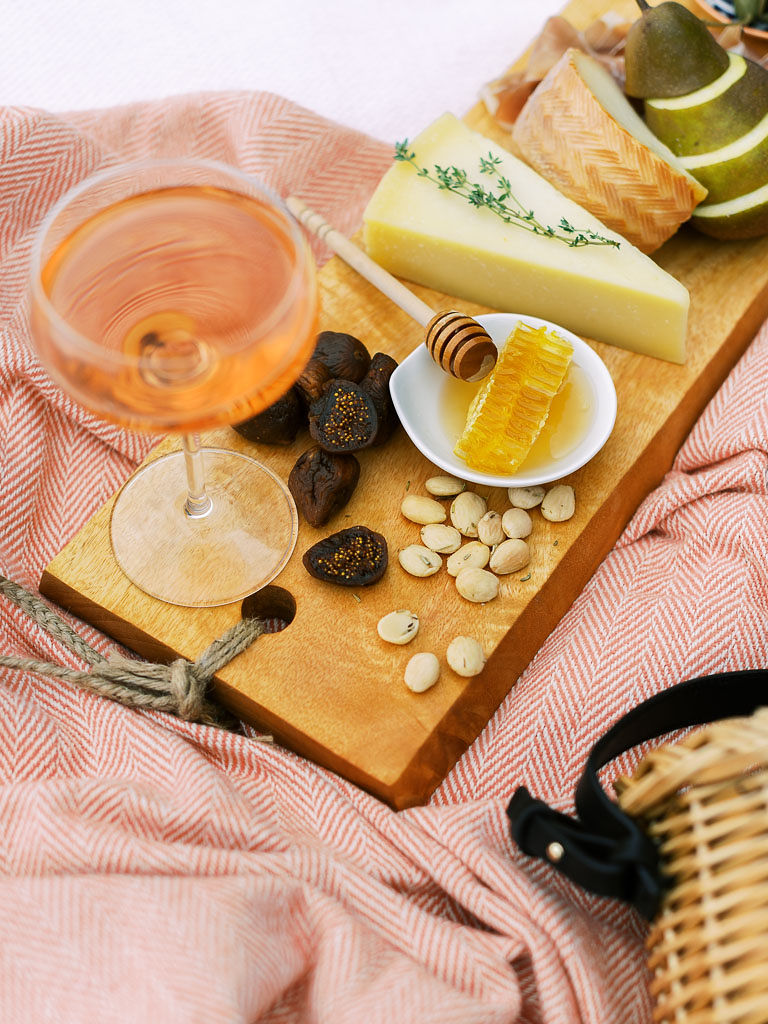 A charcuterie board with fruit, olives, cheese, meat, and nuts and a glass of rose wine on a pink picnic blanket. Photographed by Washington DC brand photographer Kim Branagan.