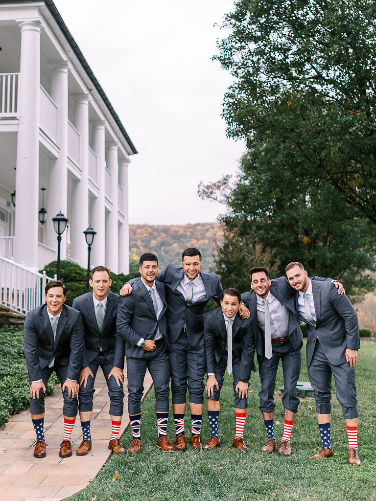 A groom and his groomsmen pulling up their pants to show off their socks, which have either the British or American flag on them,