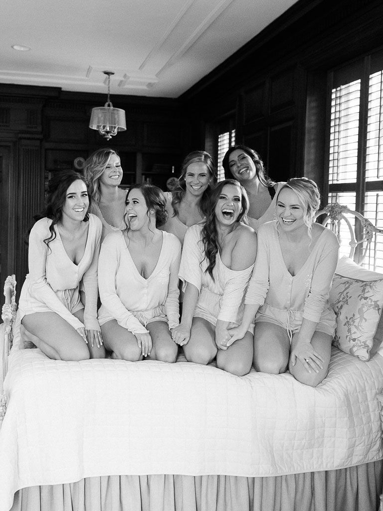 A bride and her bridesmaids sitting on a bed smiling and laughing on the bride's wedding day