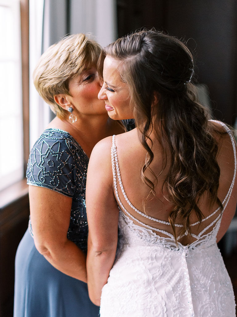The bride's mom kisses her daughter on the cheek as they get ready for the wedding. Photographed by Washington D.C. wedding photographer Kim Branagan.