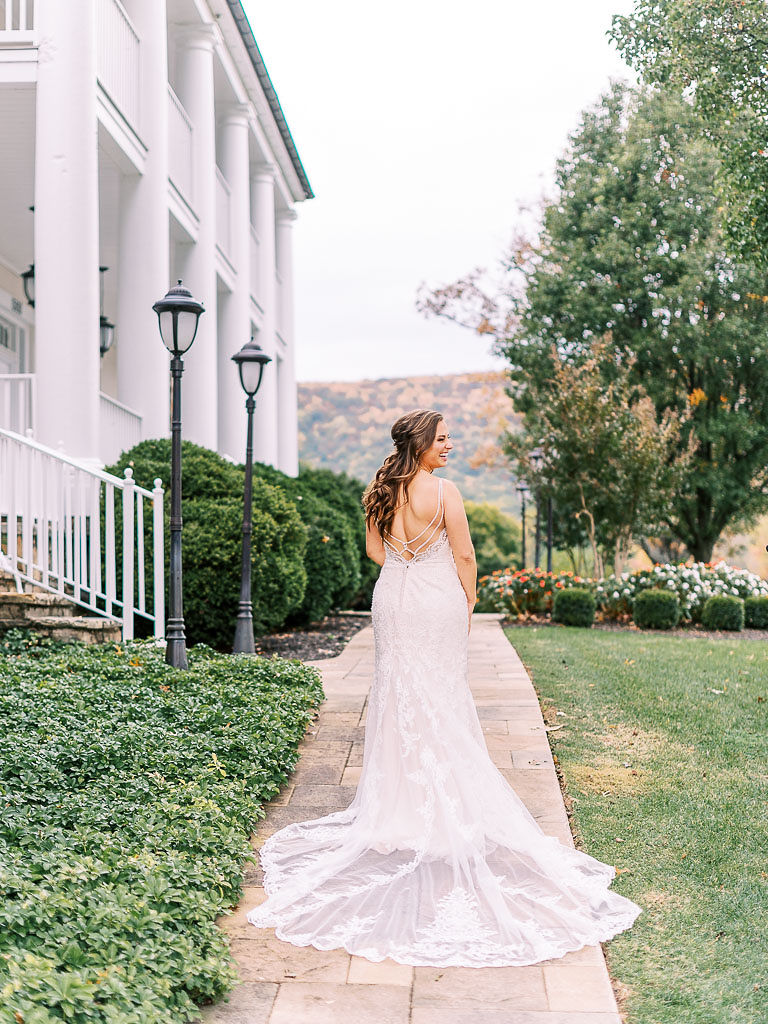 A bride stands outside on a beautiful fall day in the northern Virginia countryside. Her back is to the camera, and she is looking off to the side.