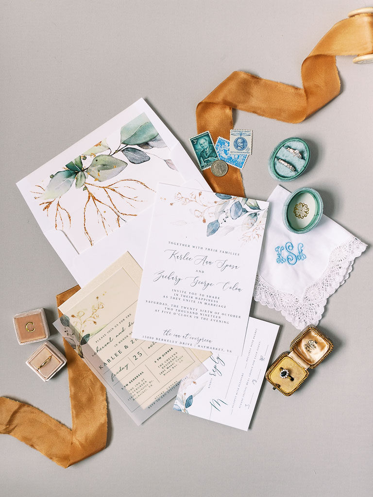 A ribbon, some vintage stamps, wedding rings, and the couple's wedding invitations on a white surface. Photographed by Virginia wedding photographer Kim Branagan