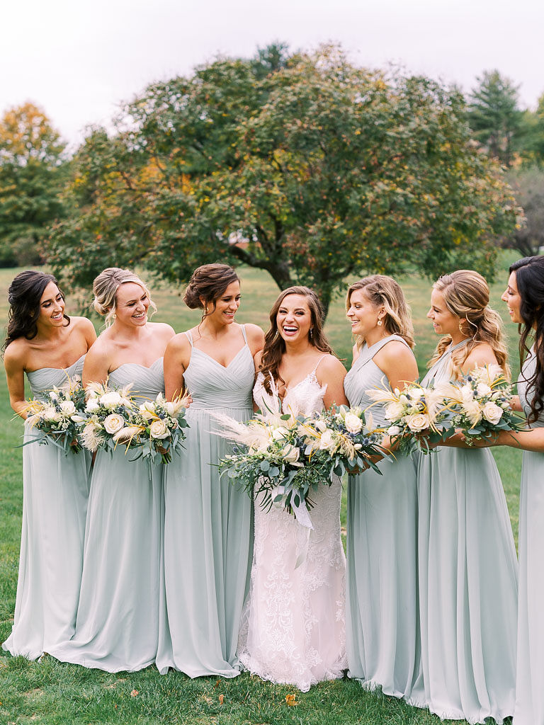 A bride and her bridesmaids on the bride's wedding day. The are holding their wedding flowers and smiling. Photographed by northern Virginia wedding photographer Kim Branagan.