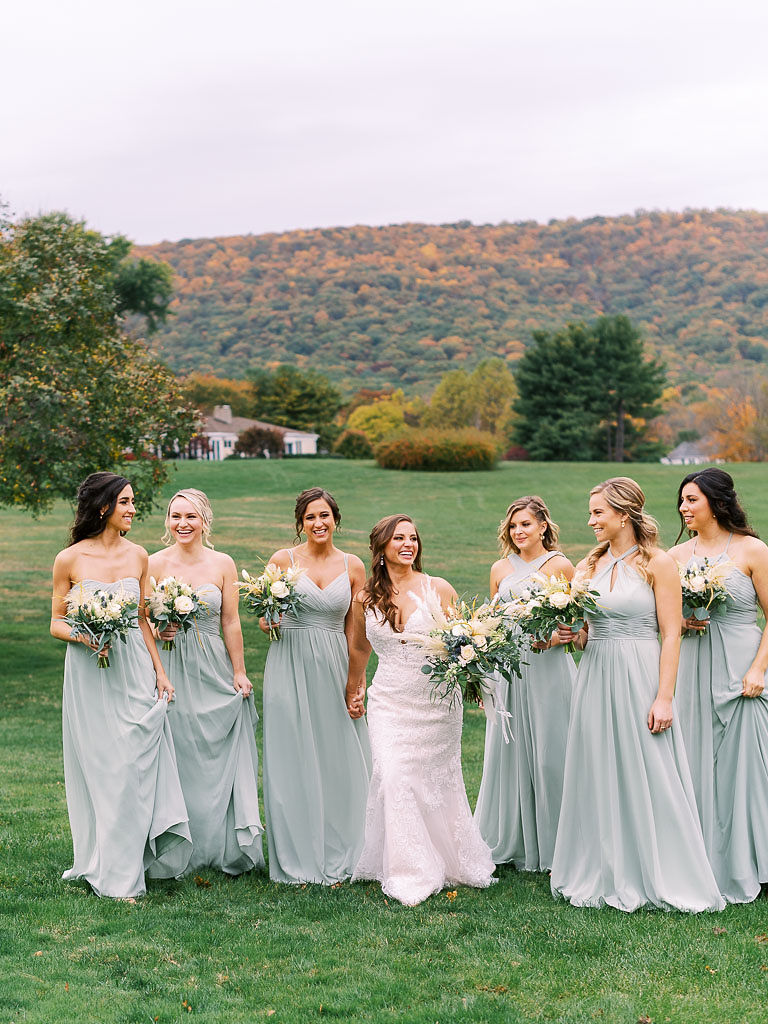 A bride and her bridesmaids hold their bouquets, walk together in the Virginia countryside and smile and laugh together.