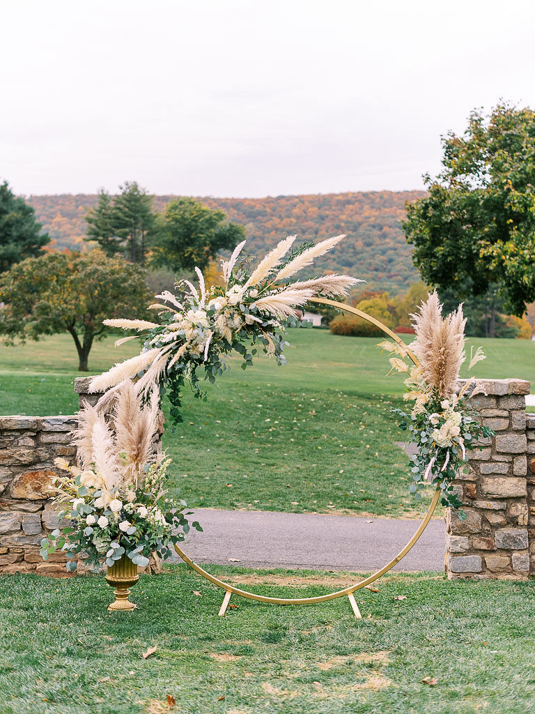 Close up shot of a large golden hoop adorned with fall florals, where the wedding ceremony will take place. Photographed by northern Virginia wedding photographer Kim Branagan.