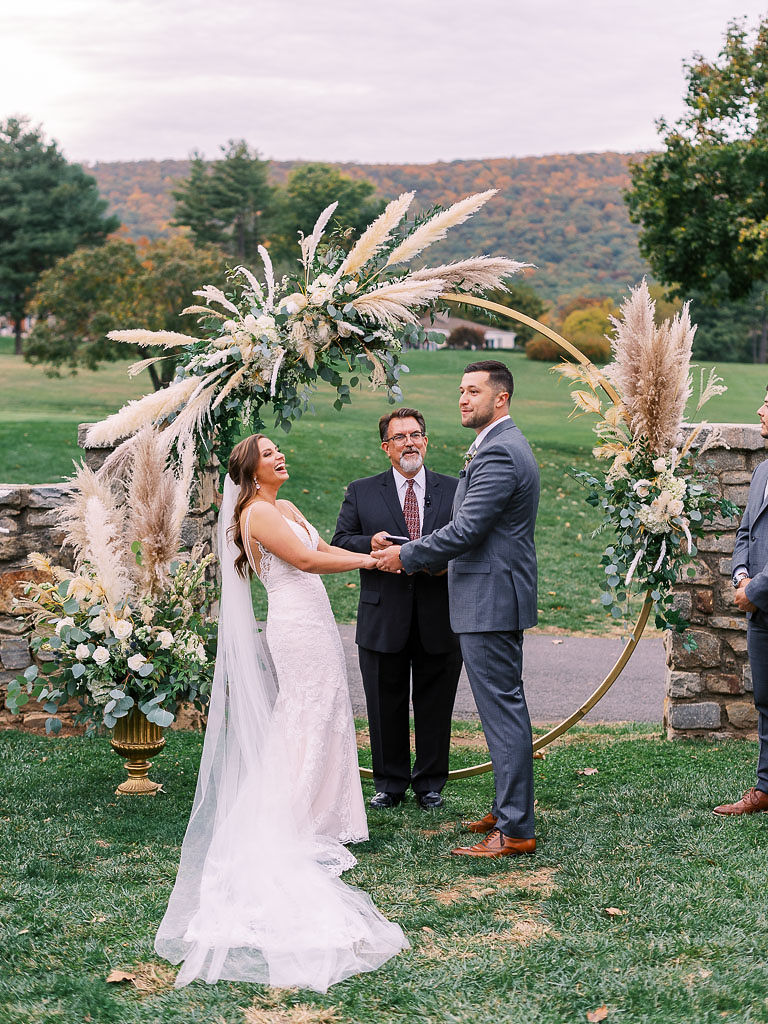 A bride and groom face each, holding hands and laughing during their wedding ceremony. Photographed by northern Virginia wedding photographer Kim Branagan.