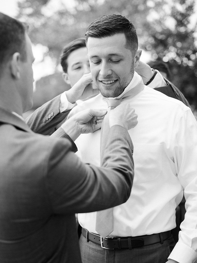 One of the groomsmen tying the groom's tie