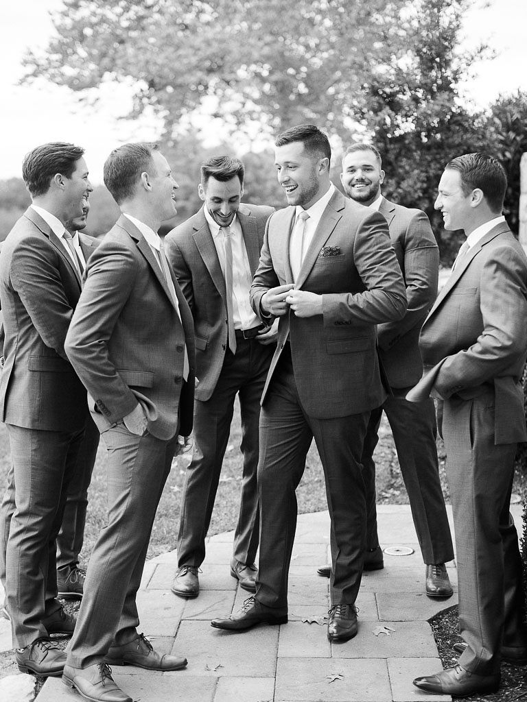 A groom on his wedding standing outside and talking and laughing with his groomsmen