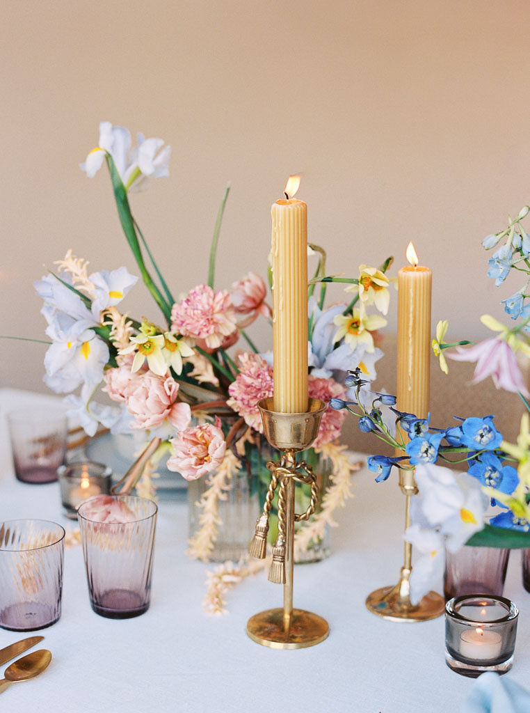 Details from a dinner table styled by Lavenders Flowers (Santa Ana.) Tall, golden-color candles and pink and blue floral bouquets make up the table's centerpieces. Individual place settings also line the table.