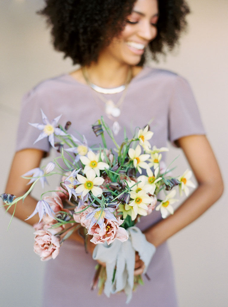 A woman at a branding editorial photo shoot smiles and looks to the ground as she holds a bouquet of bright and cheery spring flowers