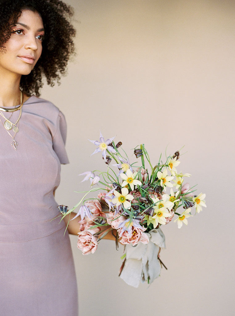 A woman stares off into the distance as she holds a bouquet of bright and cheery spring flowers in front of her