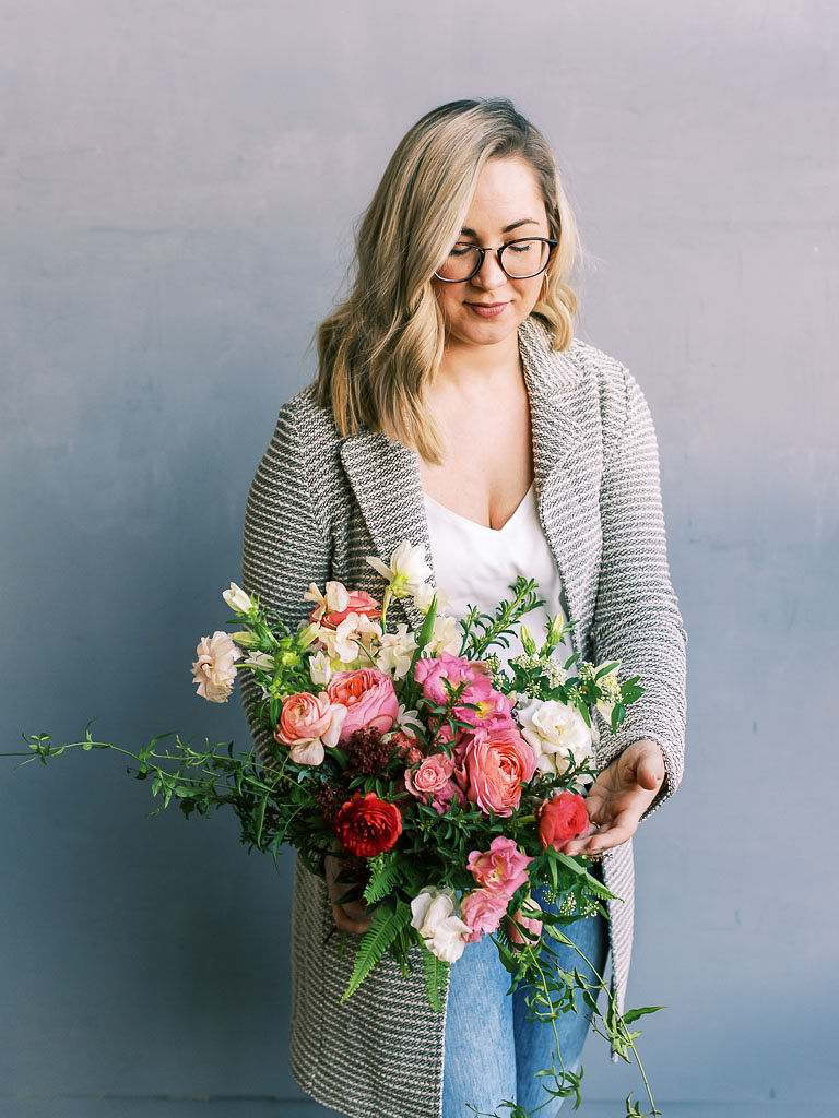 A woman stands against a gray backdrop holding the pink and blush bouquet she made at the floral workshop. Photographed by Washington D.C. event photographer Kim Branagan