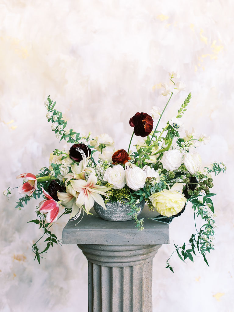 A whimsical, lush floral arrangement in a pottery vase in front of a marble backdrop at Sweet Root Village