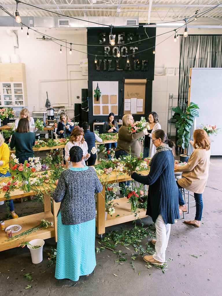 Floral workshop attendees work on designing their floral arrangements on large, wooden work tables at the Sweet Root Village studio in Alexandria, VA. Photographed by Virginia commercial photographer Kim Branagan