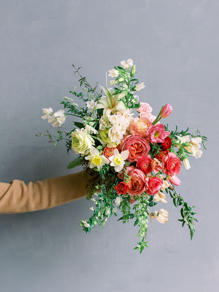 A woman's arm holds a blush, pink, and cream floral bouquet against a minimal gray backdrop. Photographed by northern Virginia floral photographer Kim Branagan