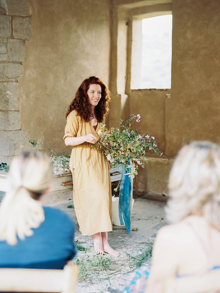 A woman in a yellow dress holds a floral arrangement she is designing as she teaches attendees of the Clarity Retreat, a floral design workshop. Clarity Retreat - A Floral Workshop by Ponderosa & Thyme | Florence, Italy. Photographed by Florence brand and editorial photographer Kim Branagan.