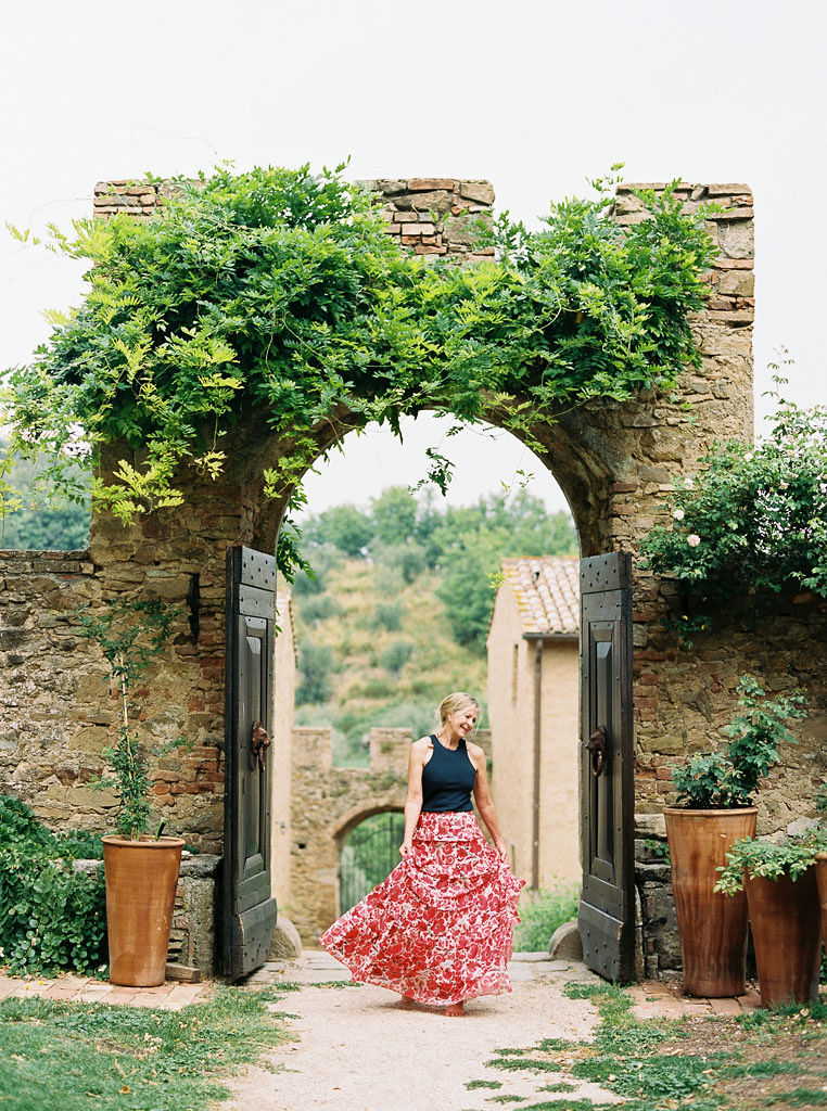 A woman wearing a long, colorful dress twirls while in front a large stone arch with moss and vines growing from it. Clarity Retreat - A Floral Workshop by Ponderosa & Thyme | Florence, Italy. Photographed by Florence brand and editorial photographer Kim Branagan.