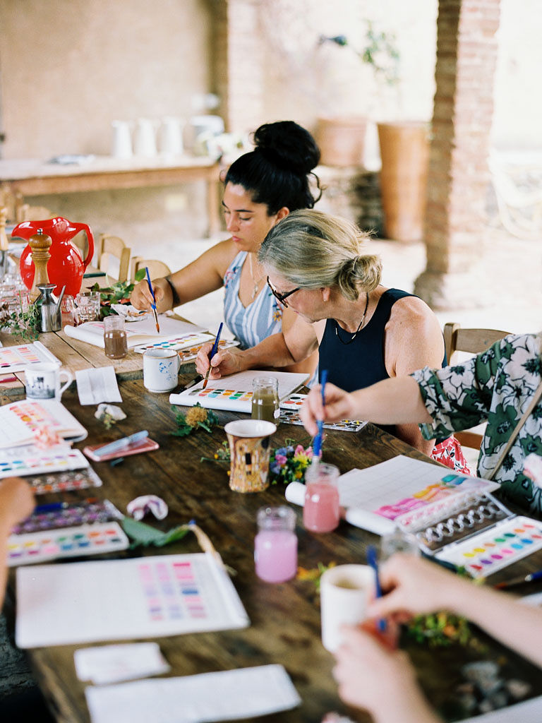 A group of people painting together at a long, wooden table. Clarity Retreat - A Floral Workshop by Ponderosa & Thyme | Florence, Italy. Photographed by Florence brand and editorial photographer Kim Branagan.