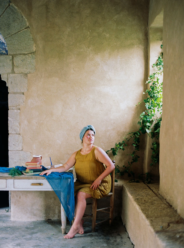 A woman wearing a dark yellow dress, sitting at a wooden table, looking out a window. Clarity Retreat - A Floral Workshop by Ponderosa & Thyme | Florence, Italy. Photographed by Florence brand and editorial photographer Kim Branagan.