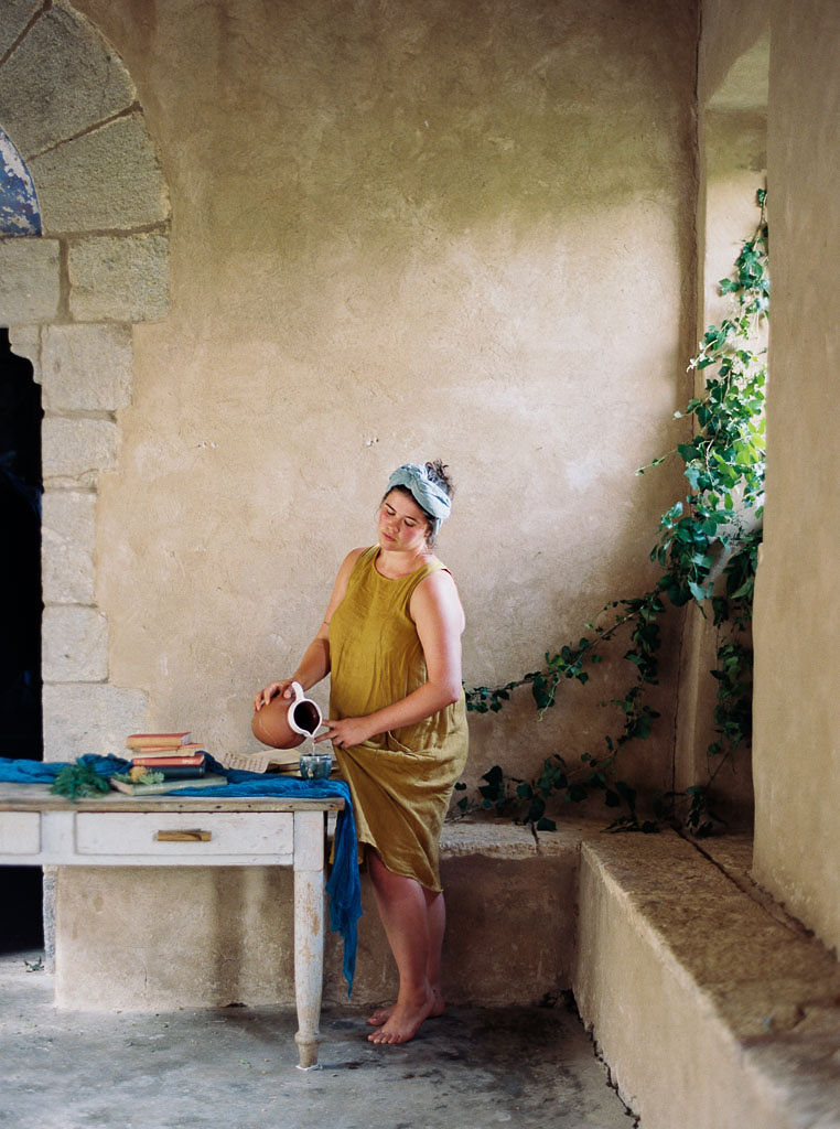 A woman standing next to a stone wall in an Italian villa, pouring water into a glass. Clarity Retreat - A Floral Workshop by Ponderosa & Thyme | Florence, Italy. Photographed by Florence brand and editorial photographer Kim Branagan.