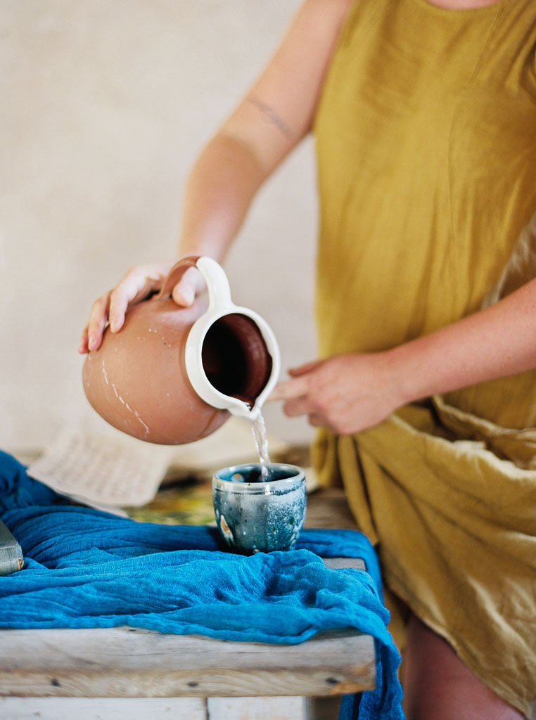 Close up shot of a woman pouring water from a ceramic jug into a ceramic cup. Clarity Retreat - A Floral Workshop by Ponderosa & Thyme | Florence, Italy. Photographed by Florence brand and editorial photographer Kim Branagan.