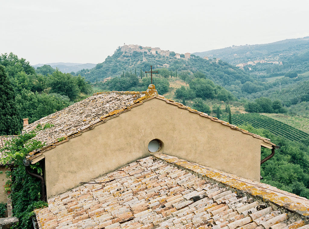 Shingles on a roof of an Italian building with a cross on top of the roof. Vineyards and orchards are in the background. Clarity Retreat - A Floral Workshop by Ponderosa & Thyme | Florence, Italy. Photographed by Florence brand and editorial photographer Kim Branagan.