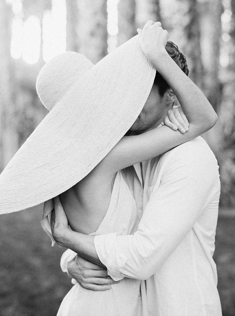 A man and woman embrace; their faces are covered by the woman's wide-brimmed sun hat. Destination Photoshoot for a Lifestyle Editorial on the Beach in San Diego, CA by San Diego lifestyle editorial photographer Kim Branagan